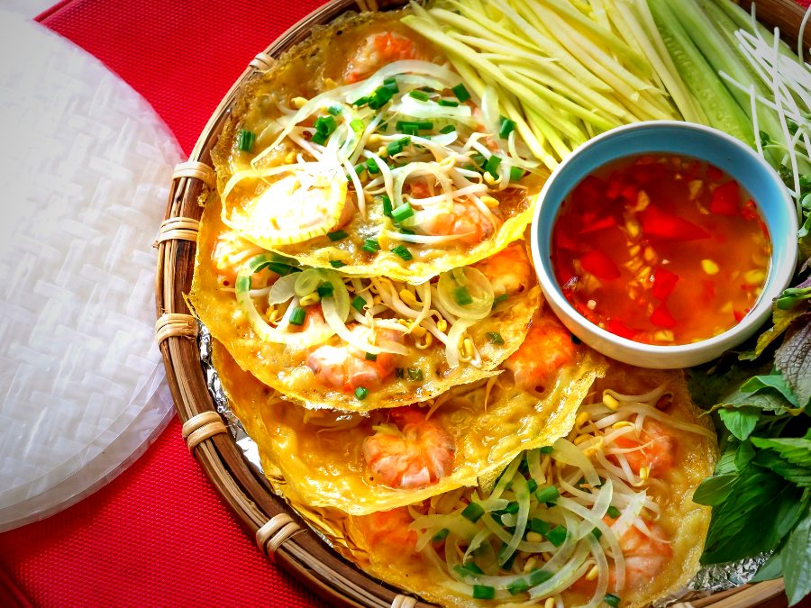 Bánh xèo tôm vàng giòn trên mẹt, kèm rau sống, bánh tráng và chén nước chấm
